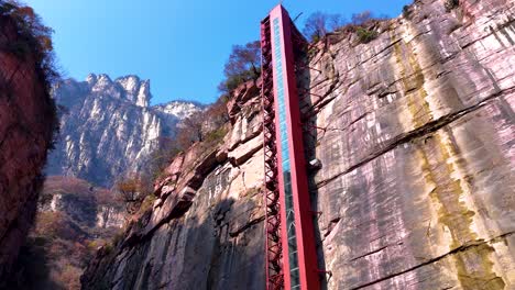 aerial showcases a towering red elevator set against the dramatic cliffs of xiuyan village, zhejiang province, china. fusion of modern engineering and natural beauty.