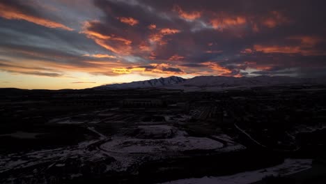 stunning sunset over a community in the valley below snowy mountains - aerial