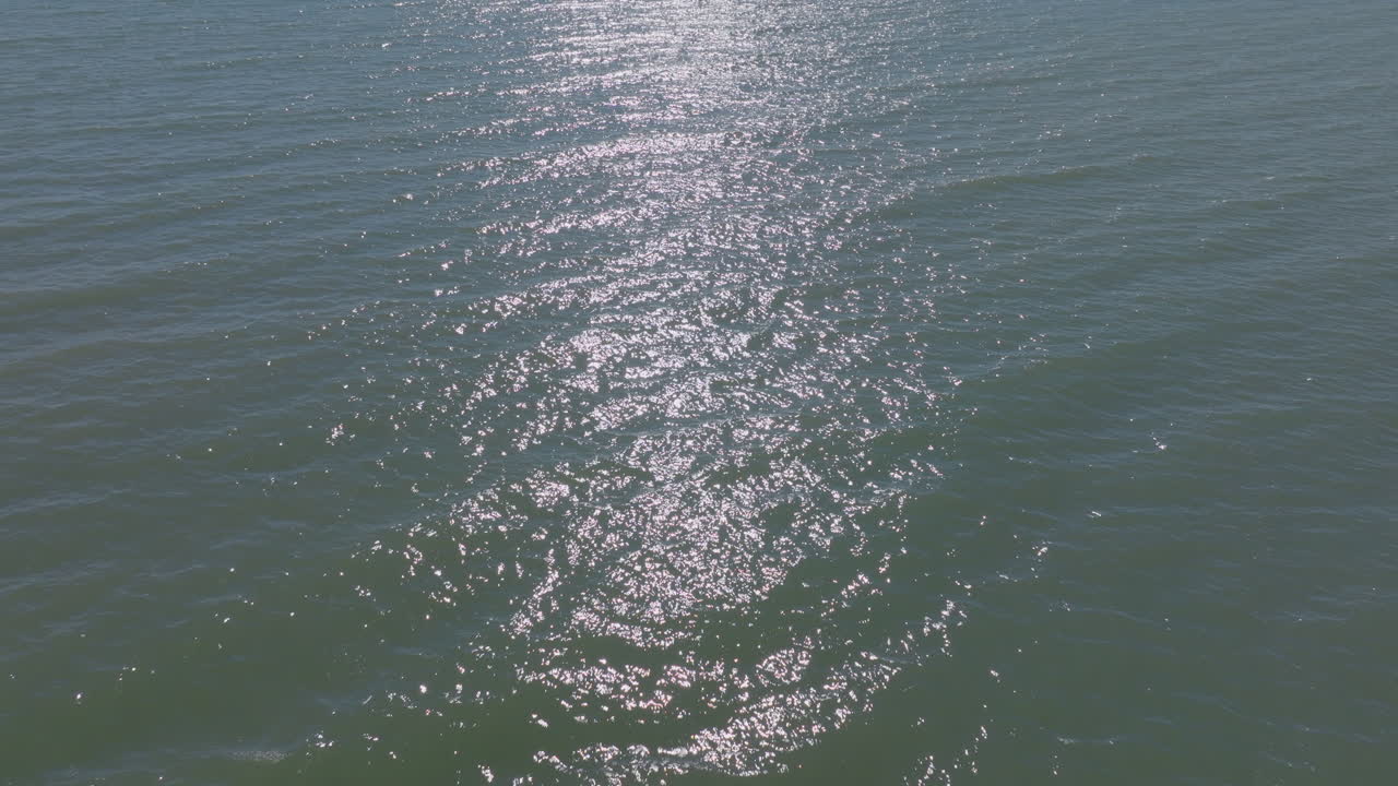 Drone aerial flying low over gentle shimmering waves in sunlight with a pullback across Lake Michigan water to reveal an old concrete pier and shoreline