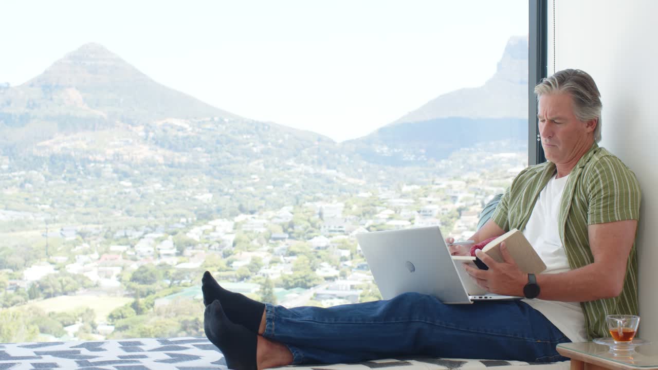 Senior man placing phone down, picking notebook, writing, typing on laptop doing work, copy space