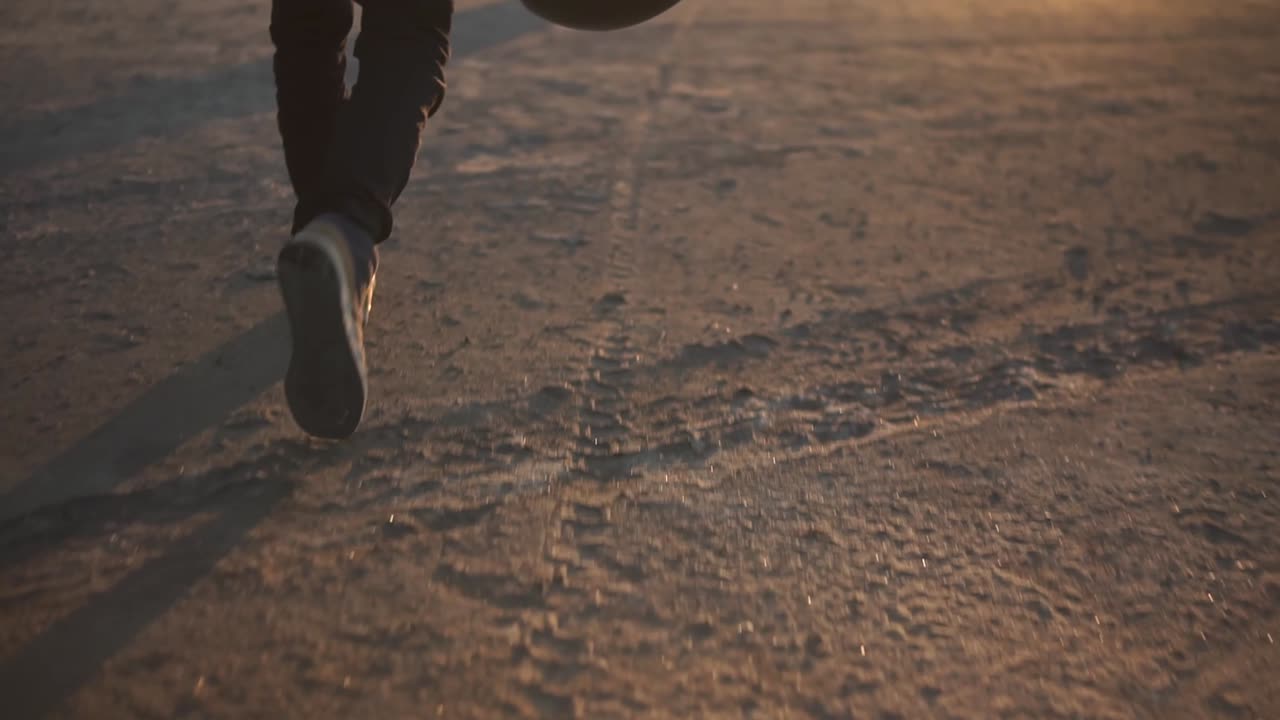 rara vista de un motociclista caminando a su bicicleta, sosteniendo su casco negro. la bicicleta negra estacionada cerca del agua