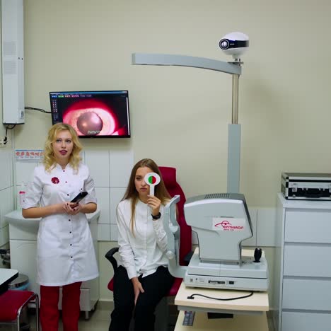 modern ophthalmological center interior. young specialist is examining woman's eyes in clinic. female patient closes her eyes in turns with occluder.