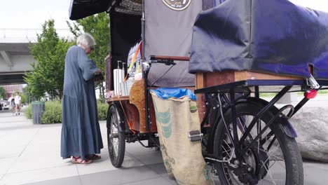 an elderly woman buys coffee at a street mobile stand on the waterfront