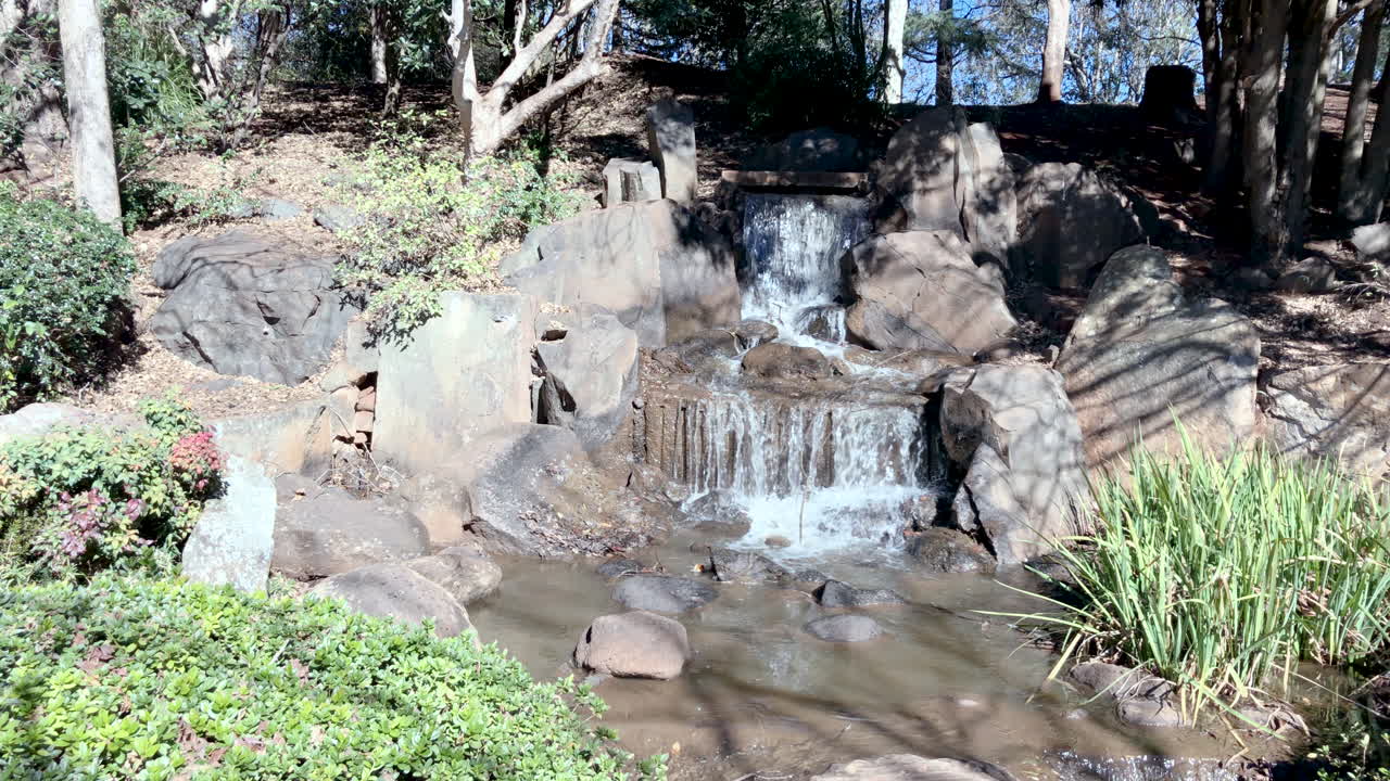 녹색 잎으로 둘러싸인 폭포의 slo-mo, ju raku en japanese garden, toowoomba, australia