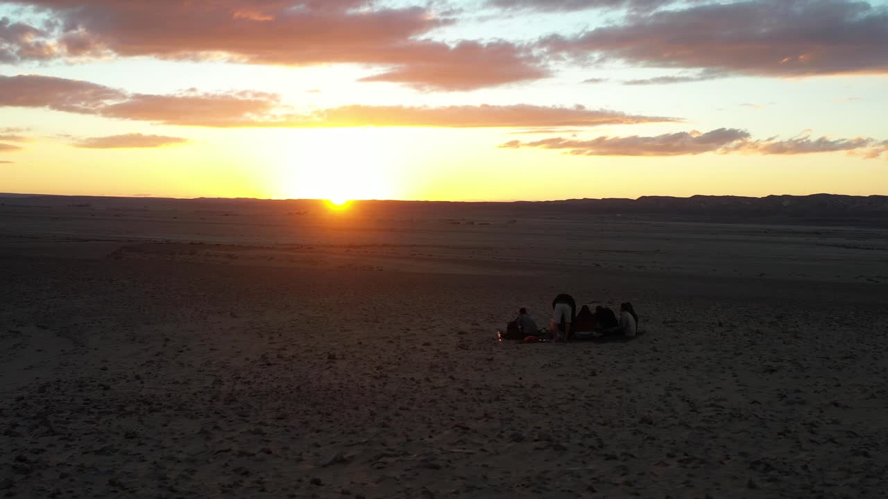 puesta de sol en el desierto tiro aéreo sobre un grupo de personas en las dunas arena ondulada en silueta seguido por una raya de luz luz del sol en la hora dorada