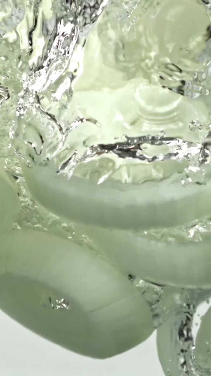 Anelli di cipolla affettati che cadono in acqua limpida con schizzi