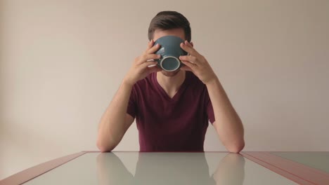 young man sitting at glass table drinking cereals in minimalistic setup indoors, still shot facing model