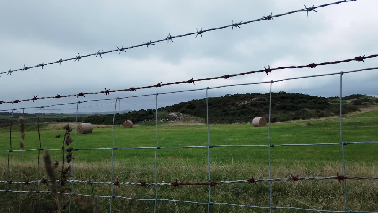 열린 흐린 영국 농지에서 압연 짚 건초 베일과 시골 와이어 울타리 초원