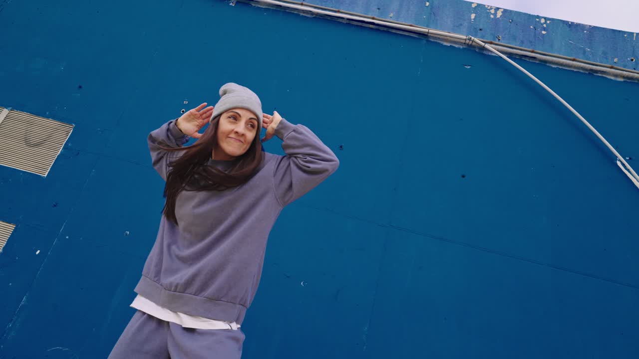Woman in casual wear dancing in front of blue wall