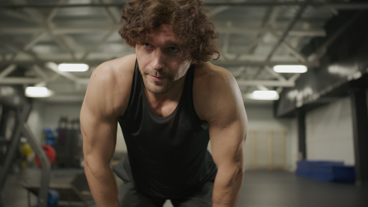Muscular Man Resting with Hands on Knees after Intense Workout in Gym