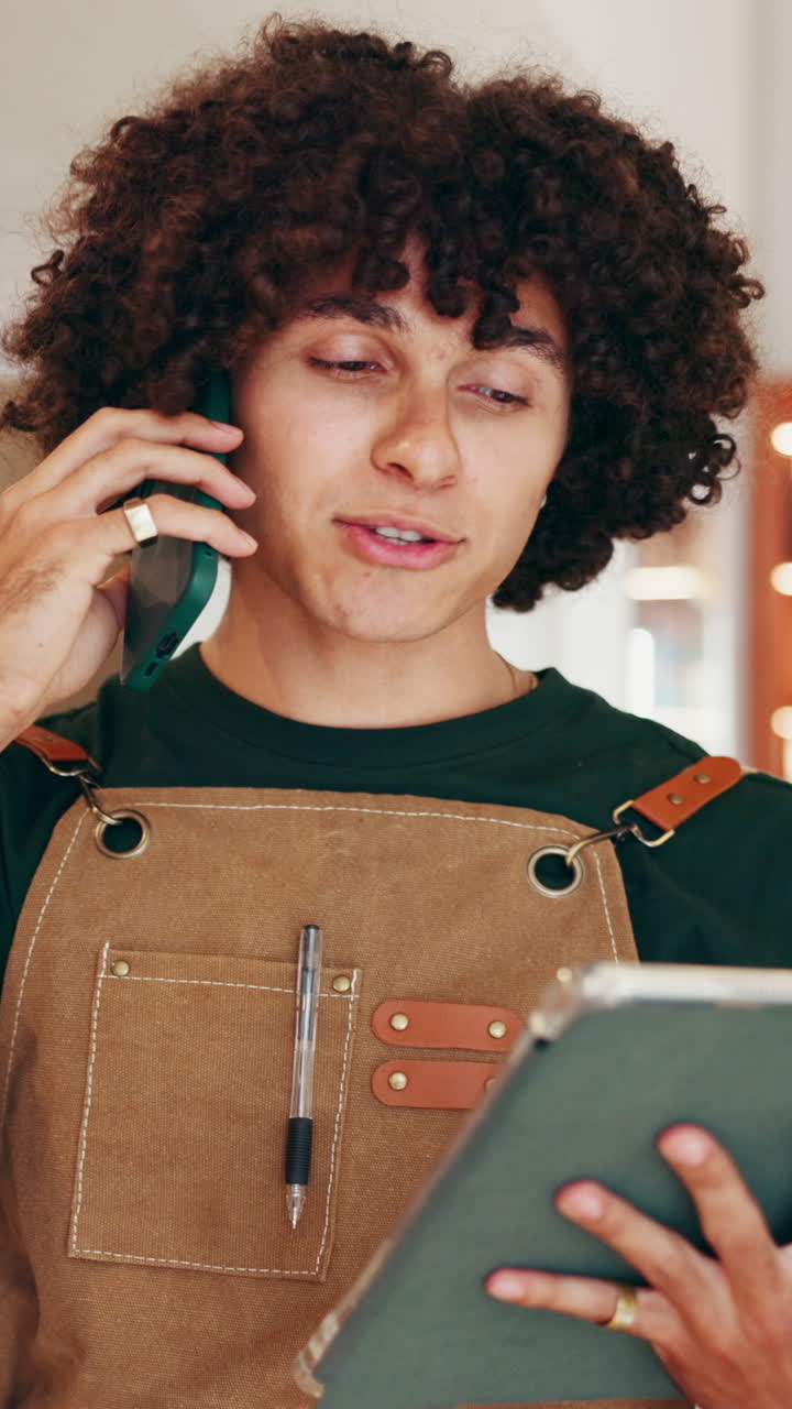 Man with curly hair on a phone call while holding a tablet