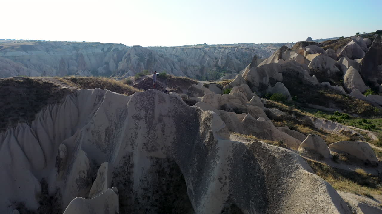 터키 카파도키아의 요정 굴뚝으로 둘러싸인 계곡 꼭대기에 서 있는 한 남자의 서사시적인 영화 드론 샷