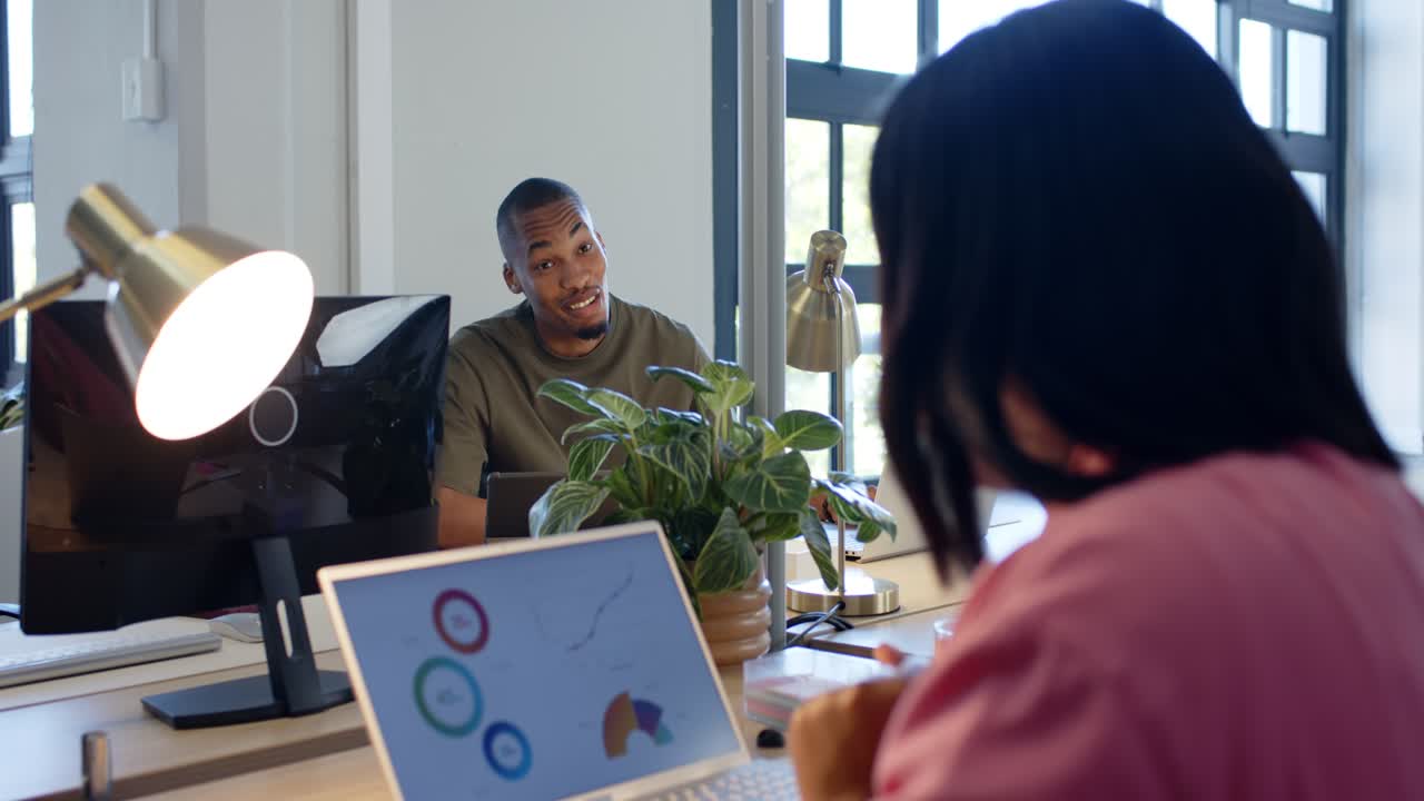 Coworkers following woman pointing at laptop charts, typing while man smiling, discussing data