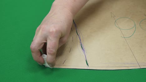 seamstress draws detail on green fabric with sewing pattern