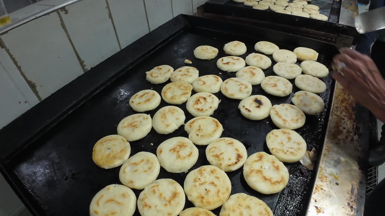 Dolly out tracking shot dari tangan yang meletakkan arepa Venezuela mentah di atas wajan panas untuk dimasak