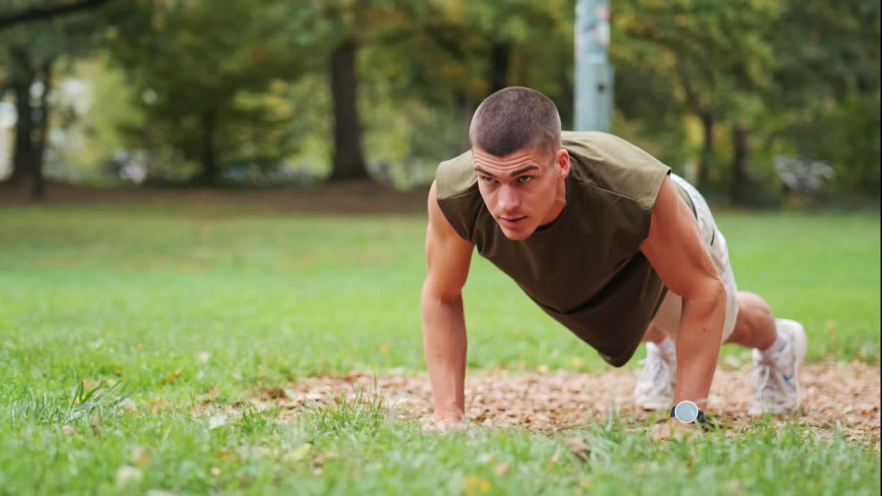 joven atlético enfocado haciendo flexiones en el área de entrenamiento del parque público, disparo de seguimiento