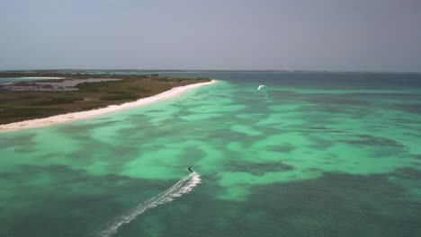 Kitesurfista-Deslizándose-Sobre-Aguas-Turquesas-Cerca-De-Una-Prístina-Playa-De-Arena-Blanca