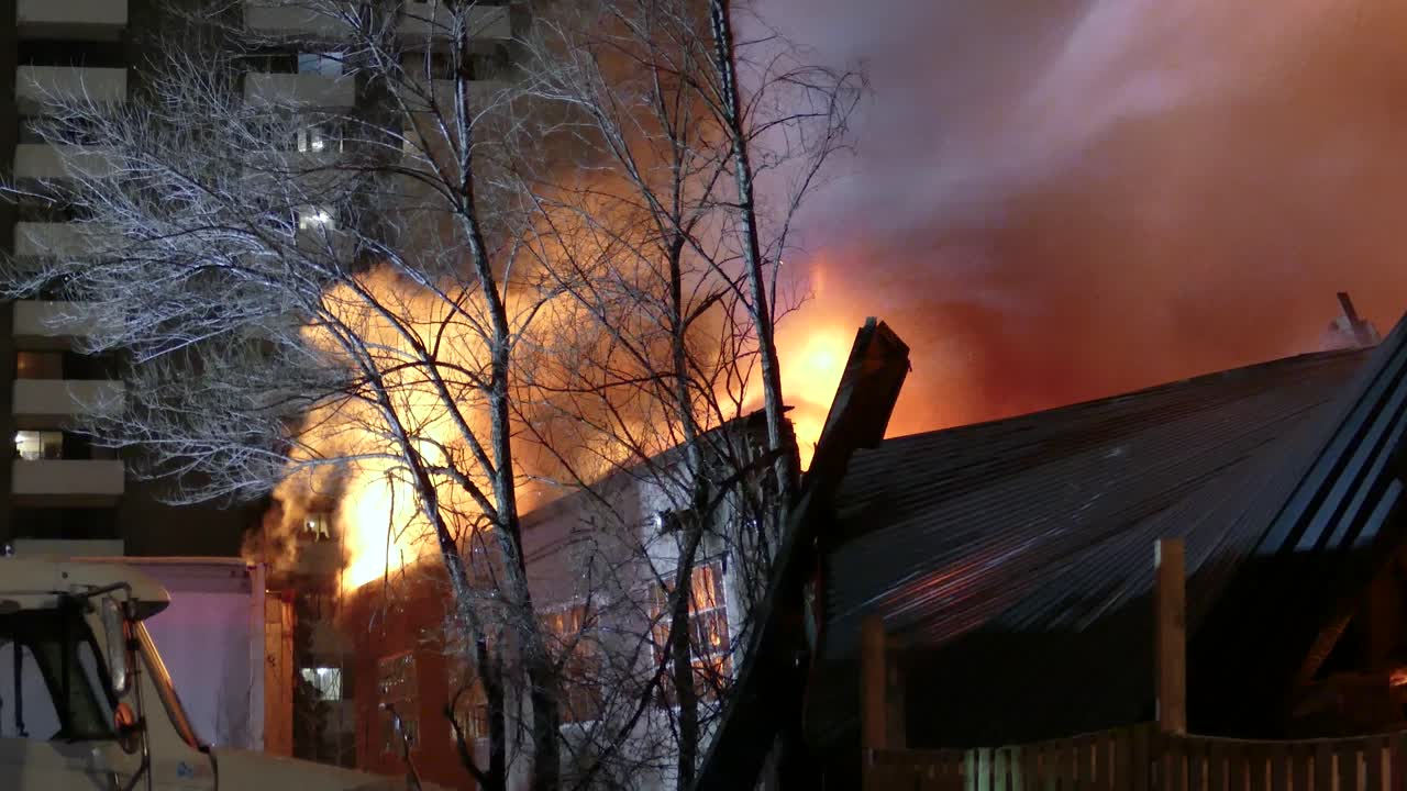 Flames engulf residential house at night with emergency lights and heavy smoke filling from water on fire
