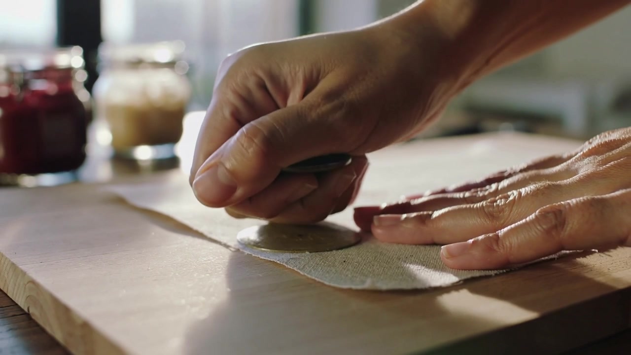 Posizionando il tagliapasta, le mani del cuoco che premono e ruotano, tagliando dischi di impasto su un tagliere di legno per la cottura