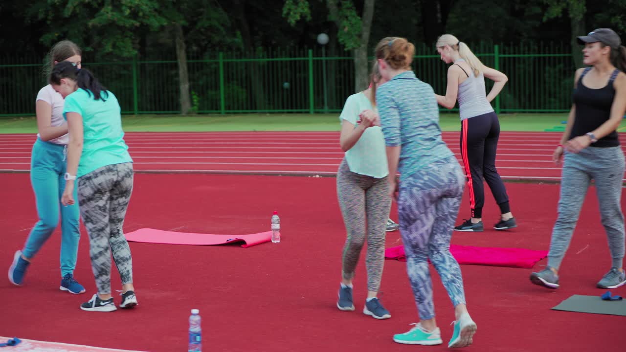 Young women doing fitness exercises in pairs outdoors. Fitness team of female in sportswear are training on the sportsground in summer.