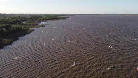 Aerial-backwards-shot-of-many-Kitesurfer-surfing-on-wavy-brown-river-at-coastline-of-Buenos-Aires