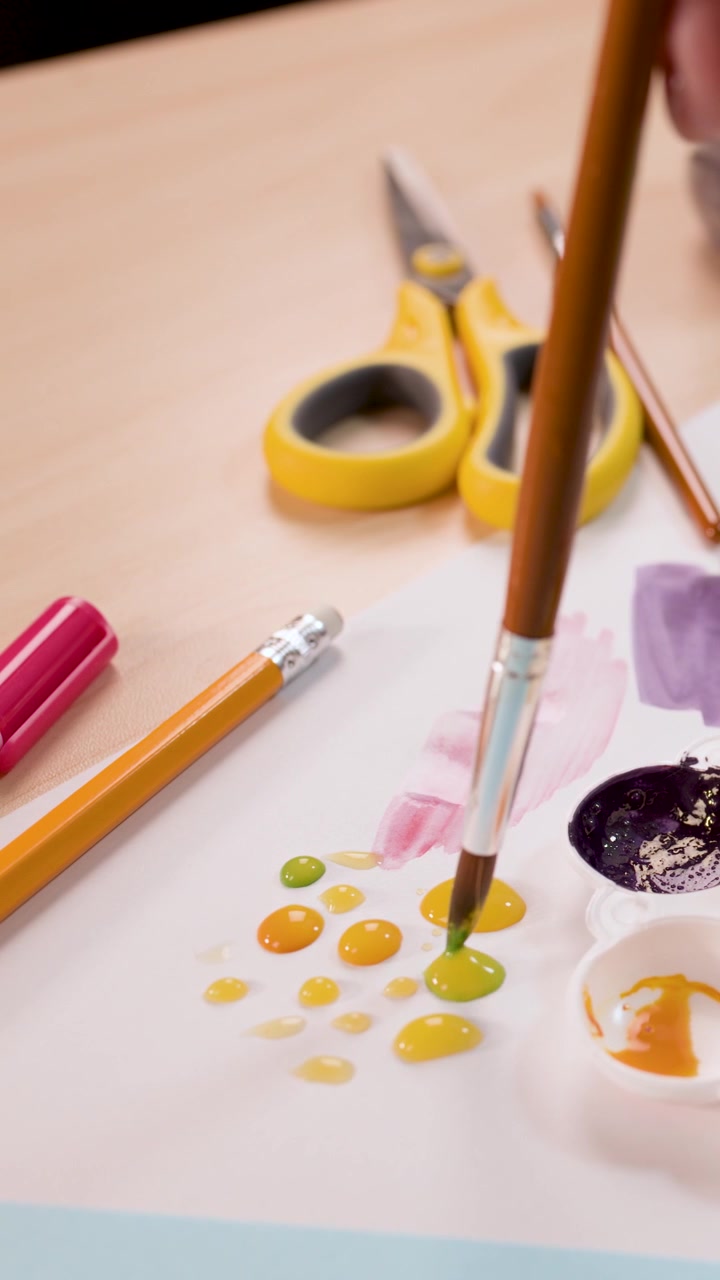 Child uses brush to mix and apply paint on paper in bright, organized craft workspace