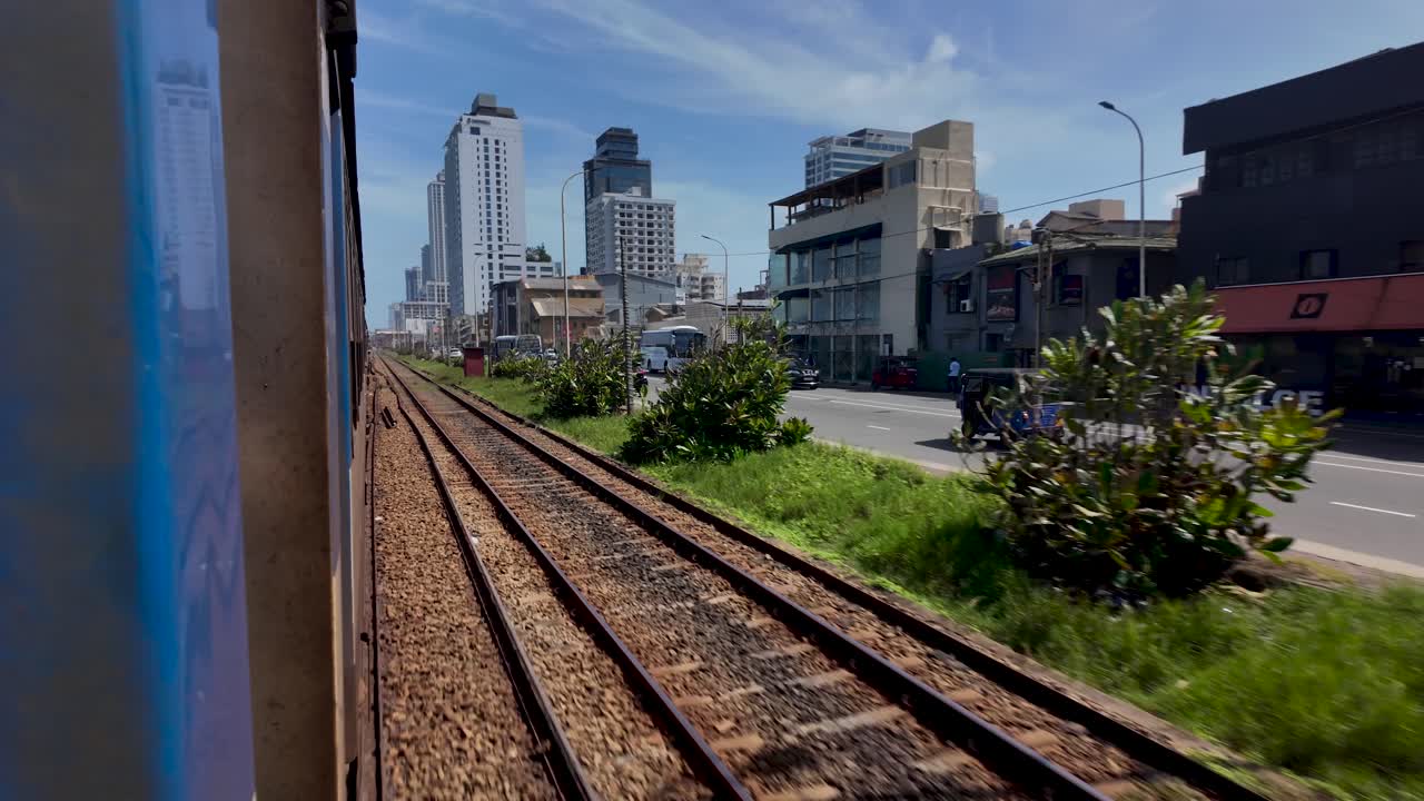 Experience the bustling urban landscape of Colombo through a train window, capturing city buildings and a roadside journey. Perfect for travel and adventure enthusiasts.