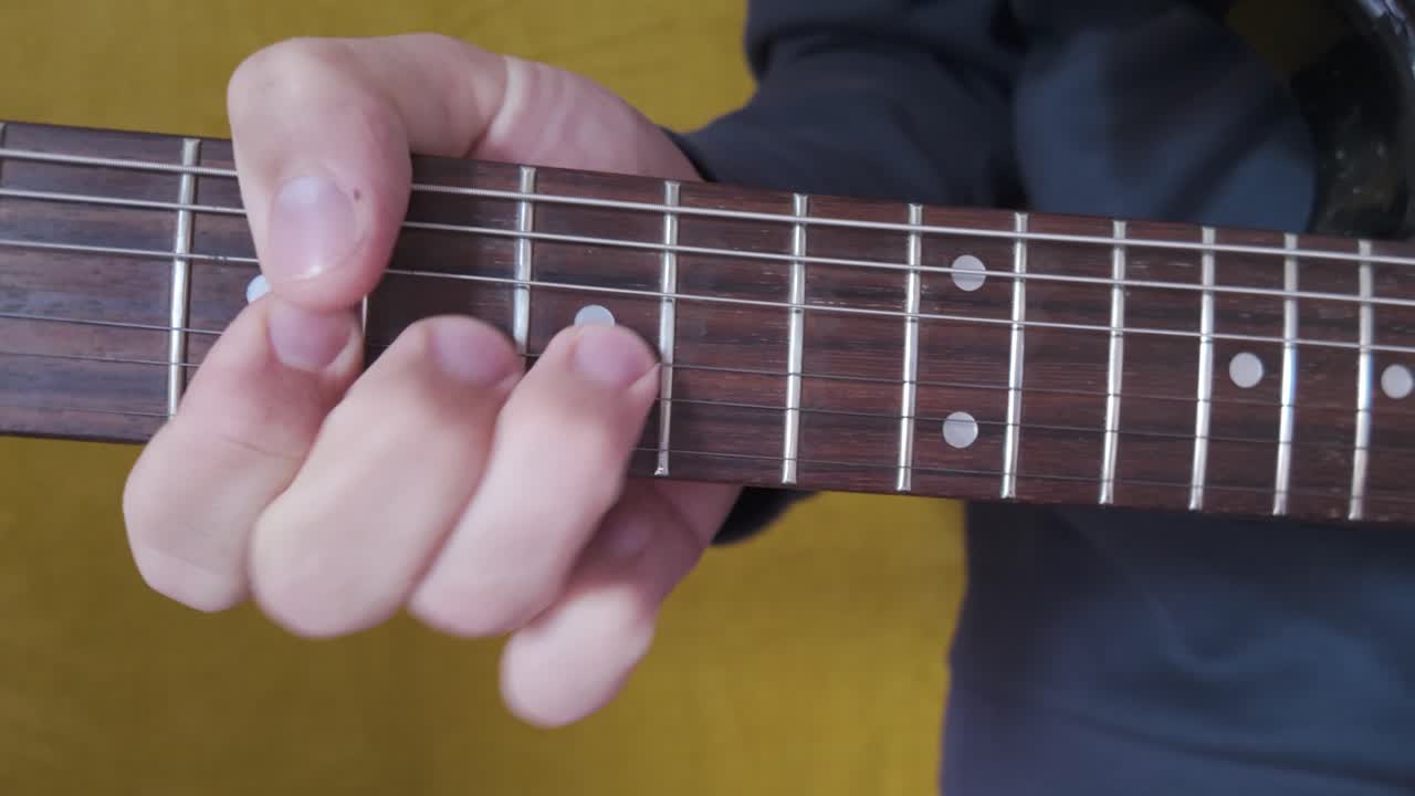 Close up of a person playing an electric guitar, focusing on hand movements and strumming technique in detail