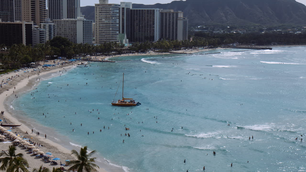 Catamarano giallo che salpa contro le onde, circondato da folle di bagnanti, Hawaii, campo lungo