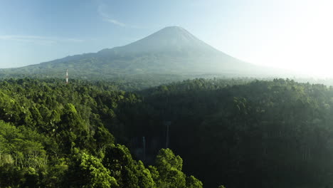Aerial-view-over-rainforest-tilting-toward-the-Tumpak-Sewu-waterfall,-in-sunny-Indonesia