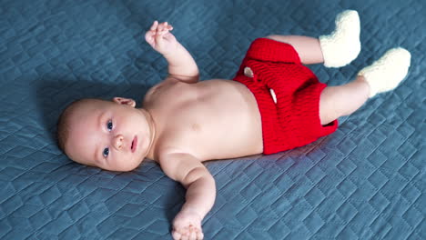 adorable healthy baby put on the bed in pants and socks only. boy tossing his feet and is ready to express his annoyance. grey backdrop.
