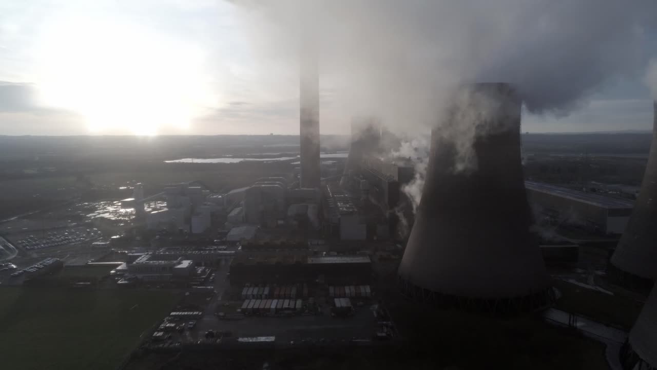 Aerial lowering pull back UK power station cooling towers below smoke steam emissions at sunrise