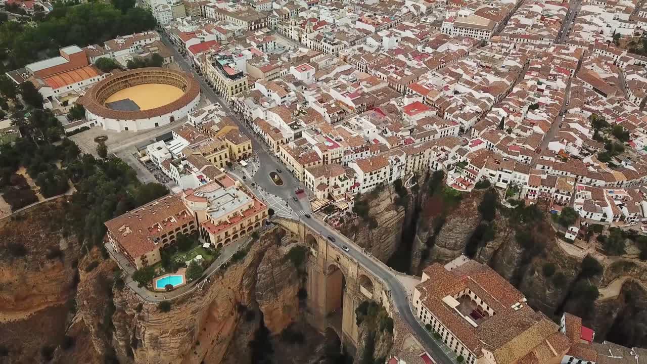 A breathtaking aerial perspective of Ronda, Spain, highlighting the iconic Puente Nuevo bridge spanning a deep gorge, traditional buildings, and the circular bullring amidst the picturesque landscape