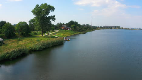 drone-view-of-small-dock,-pier-near-the-river-with-fields-in-the-background