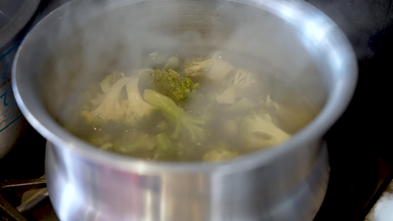 Primo piano di cimette di broccoli che bollono in una pentola d'argento con vapore che si alza