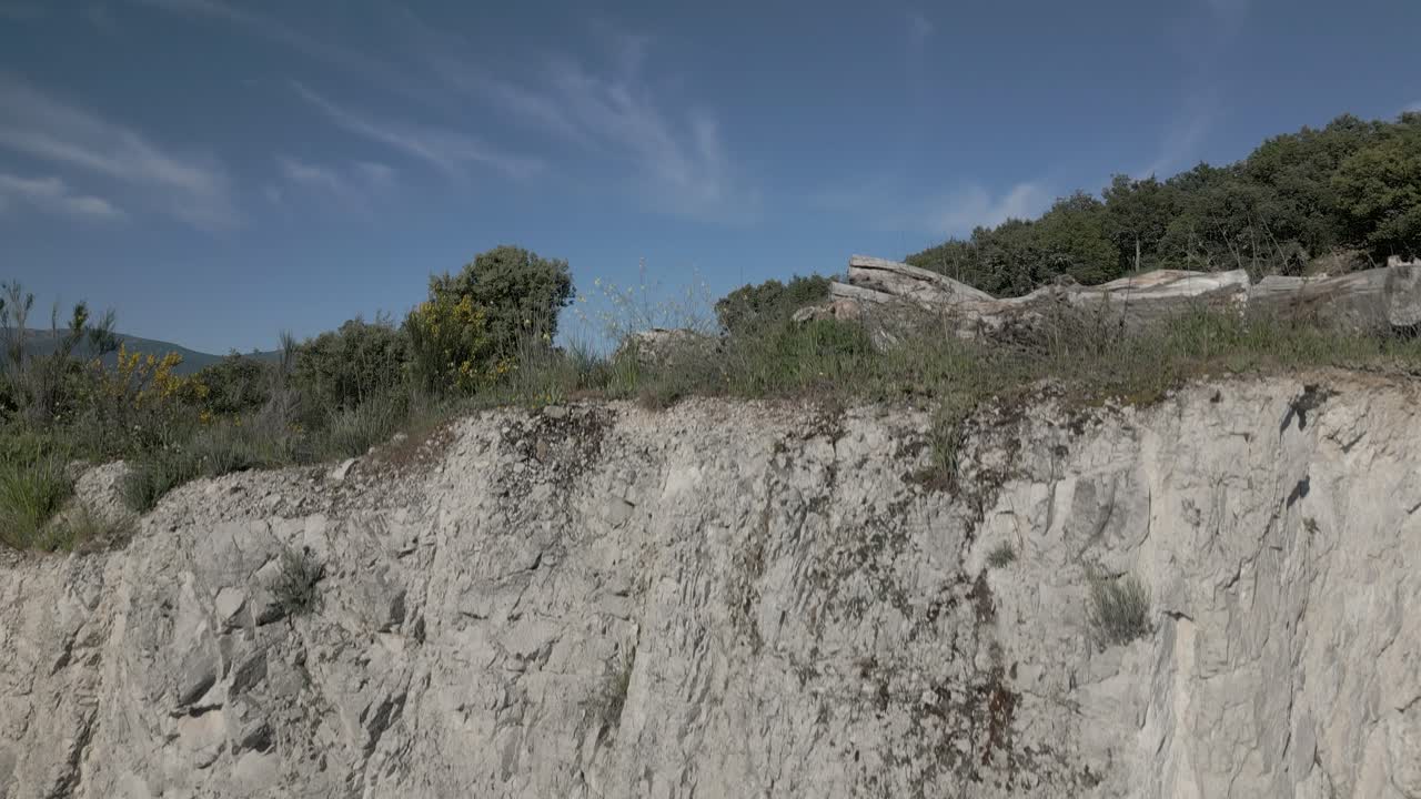 vuelo ascendente con un dron con un efecto sorpresa comenzando en una pared de tierra blanca y descubriendo algunos troncos en un camino rural en un hermoso paisaje con montañas en el fondo avila españa