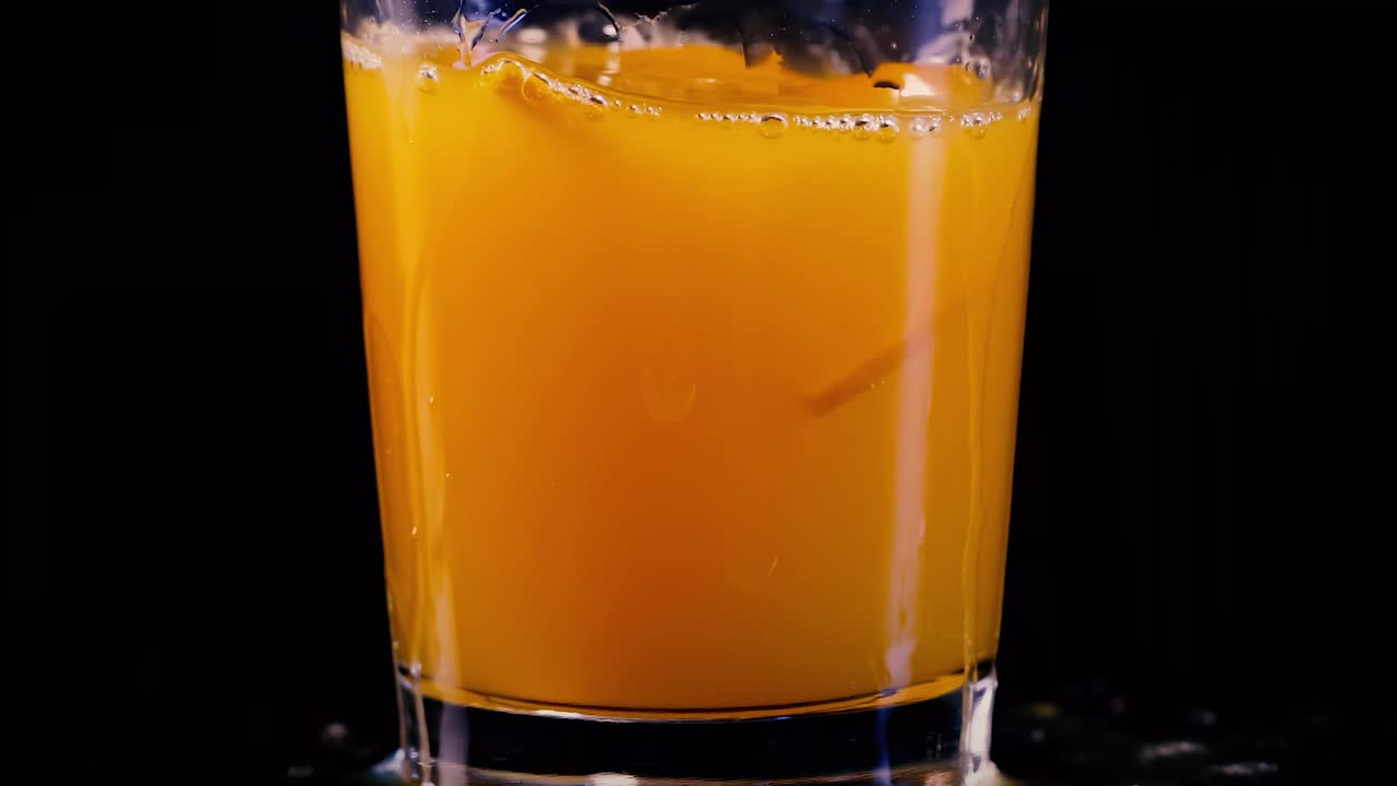 Close-up of orange juice rippling in a glass against a dark background, showcasing dynamic liquid motion.