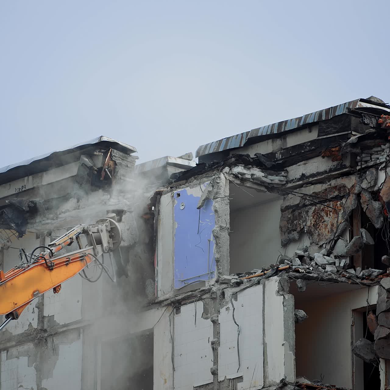 Excavator claw breaks the parts of ruined building. Dangerous deconstruction site with falling debris. Demolishing of the upper floors