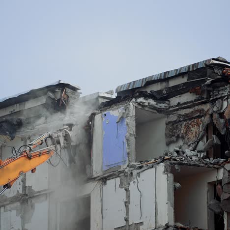 excavator claw breaks the parts of ruined building. dangerous deconstruction site with falling debris. demolishing of the upper floors