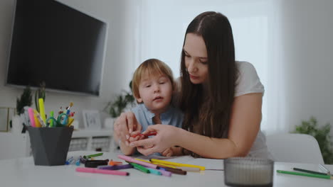 a family of one children boy and a young mother sitting at the table draws on paper with colored pencils. development of creativity in children.