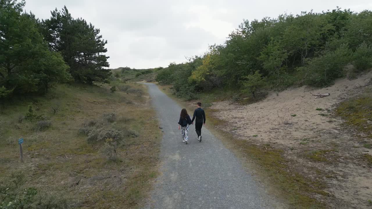 Aerial drone shot of a man and woman walking hand in hand through Dutch coastal dunes