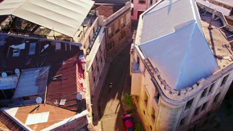 Cinematic-tilt-up-aerial-view-of-a-cyclist-passing-through-the-cobblestone-streets-of-the-Concha-y-Toro-neighborhood-at-sunset,-Santiago-Chile,-Walker-Palace