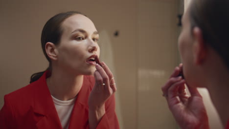 lady applying red lipstick in mirror reflection closeup. confident girl makeup