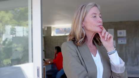 thinking deeply, senior woman in casual attire standing near open door, in office