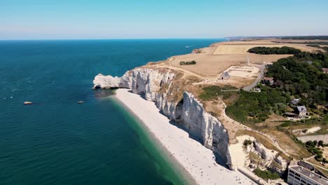 toma panorámica aérea de famosos acantilados con playa de arena y mar azul en etretat, francia - campos agrícolas en segundo plano a la luz del sol