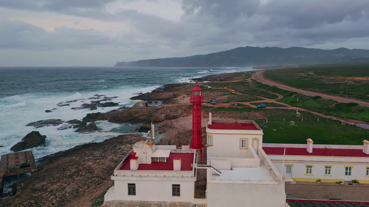Coastal scene red lighthouse at stormy evening weather drone view. Ocean waves