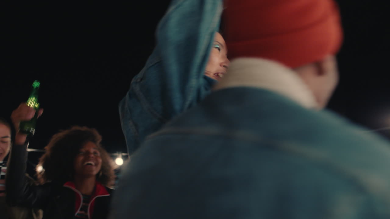 젊은 그룹 친구들이 즐겁게 놀이로 함께 춤을 추고 밤에 옥상 파티를 즐기고 웃으며 우정을 축하합니다.