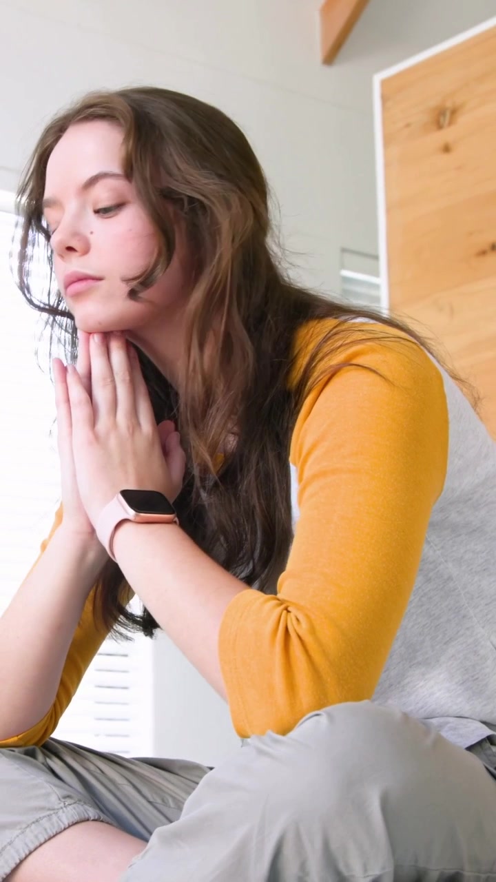 Video verticale: Fermandosi, donna con top color senape che si strofina la testa, coprendosi il viso sul letto, turbata, smartwatch.