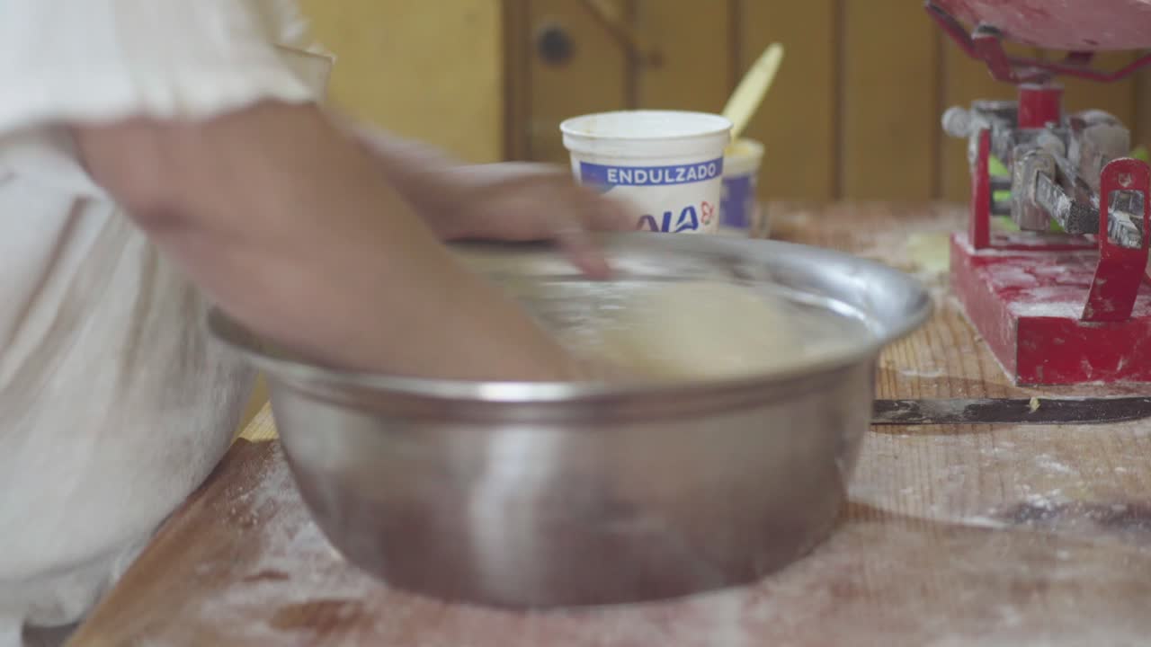 primer plano de un chef de pastelería mezclando vigorosamente la masa en un gran cuenco de metal para hornear