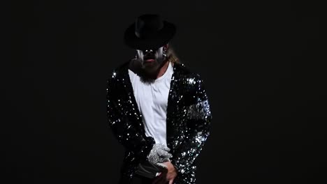man in sequin jacket and black hat performing against a dark background